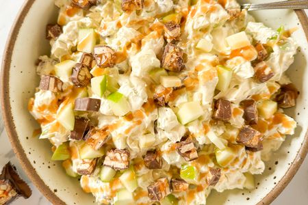 A bowl of Snickers salad with chopped apples, Snickers pieces, and caramel drizzle, served in a ceramic dish