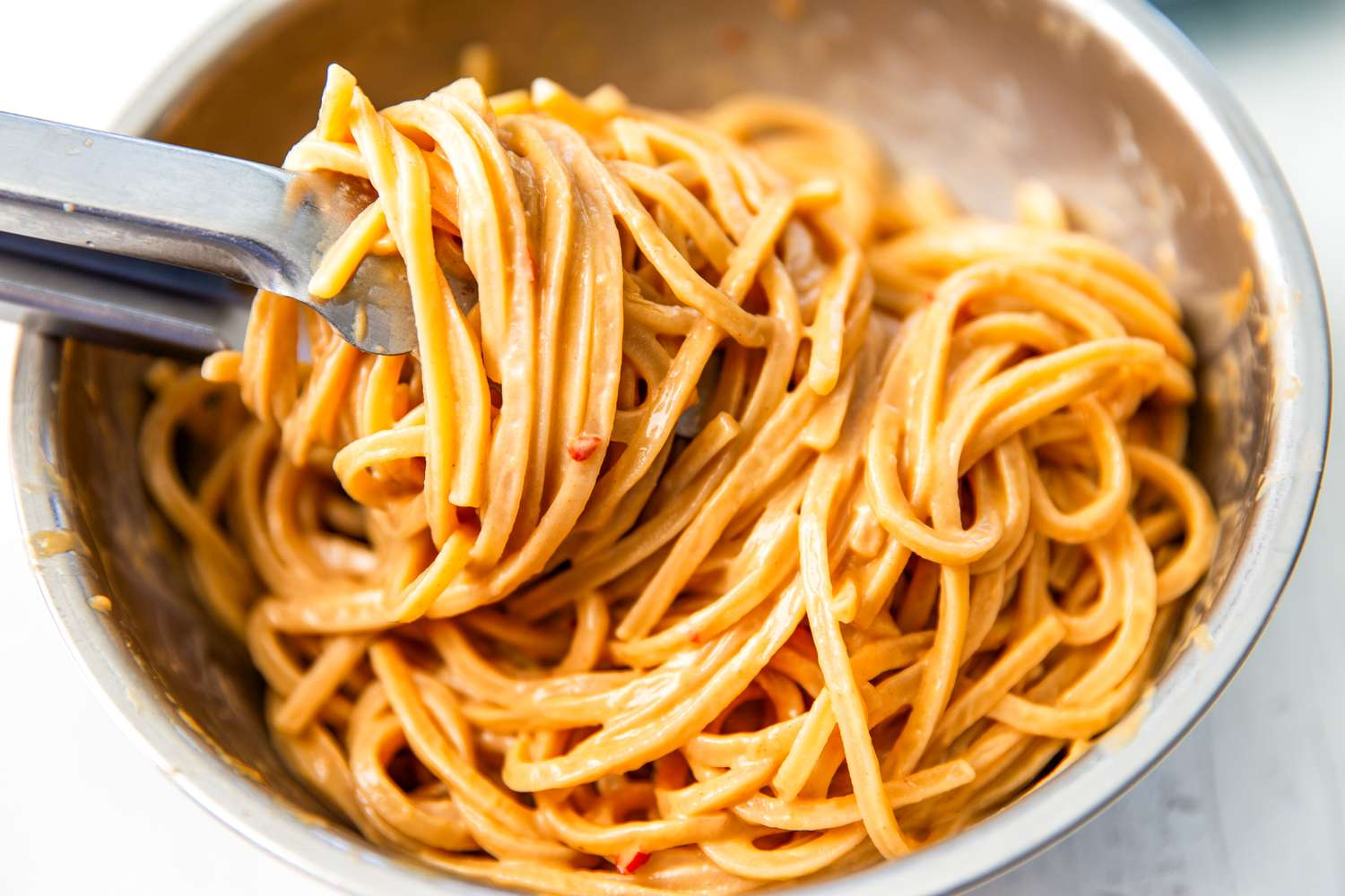 Bowl of noodles with a peanut butter sauce being stirred with tongs