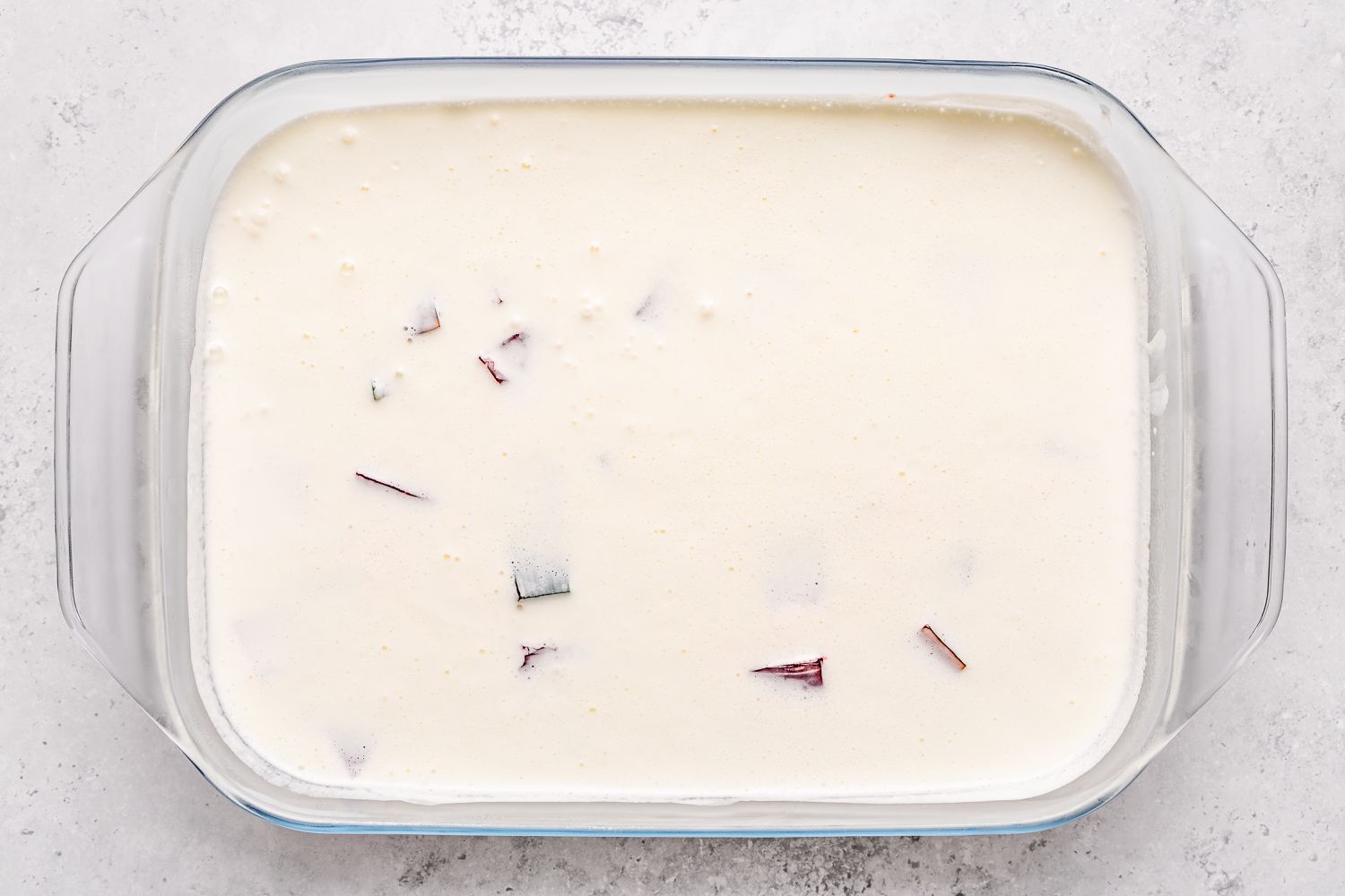 Overhead shot of a rectangular clear baking dish with jello squares and cream poured on top for the stained glass jello recipe