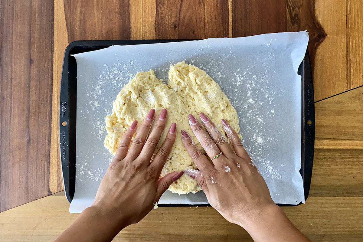 Hands pressing dough into a parchment lined baking sheet to show how to make gluten free cinnamon rolls.