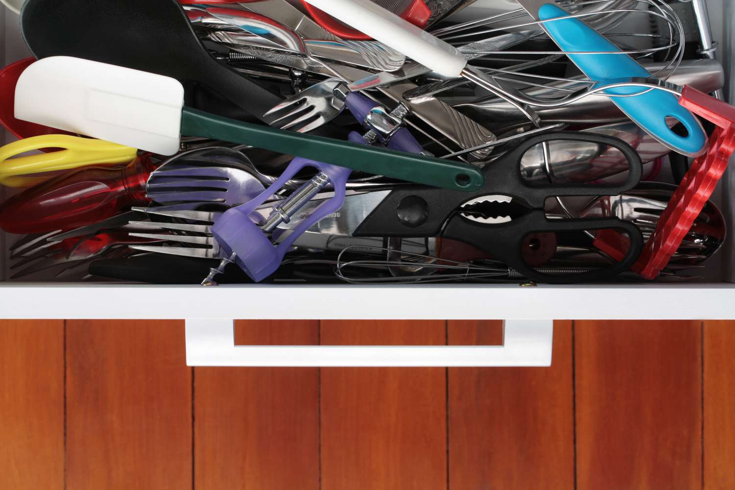 An open kitchen utensil drawer showing a messy pile of utentils and cooking tools