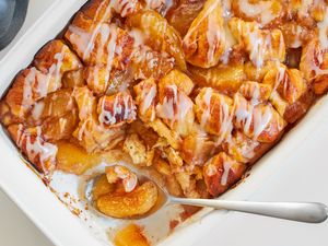 A baked apple cinnamon cobbler with icing in a white casserole pan a serving spoon scooping a portion from one end