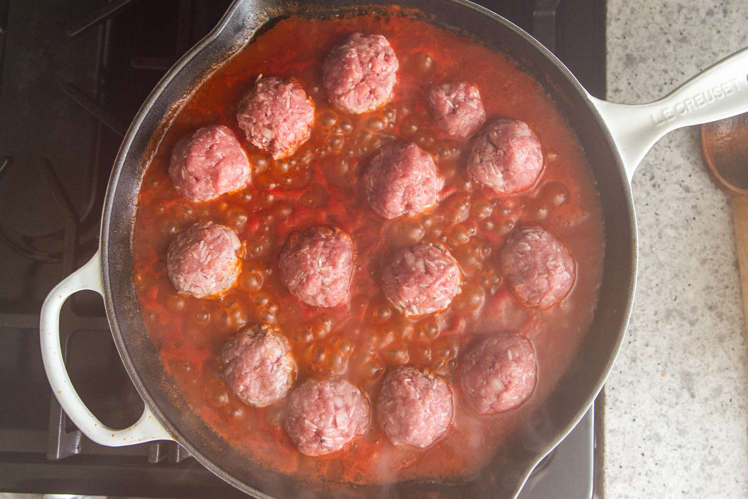 Overhead view of a cast iron skillet on a gas stove after adding meatballs for Easy Porcupine Meatballs recipe