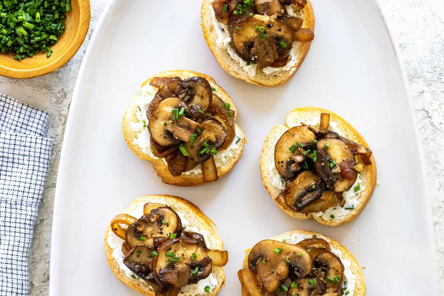 Overhead view of crostini topped with savory mushrooms and caramelized onions on a white platter.