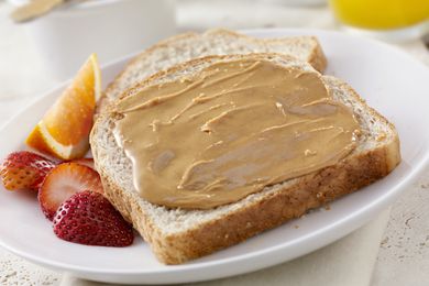 Toast with peanut butter strawberries and orange slices on a white plate