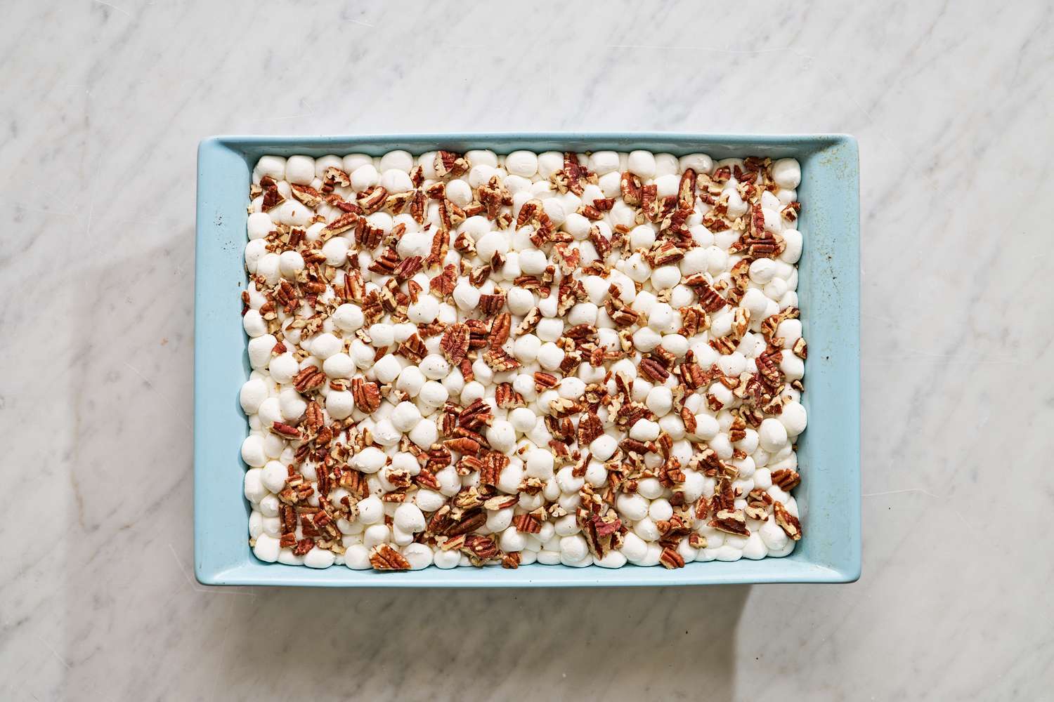 Overhead view of a light blue baking dish of the batter after topping with marshmallows and pecans for Mississippi Mud Cake recipe