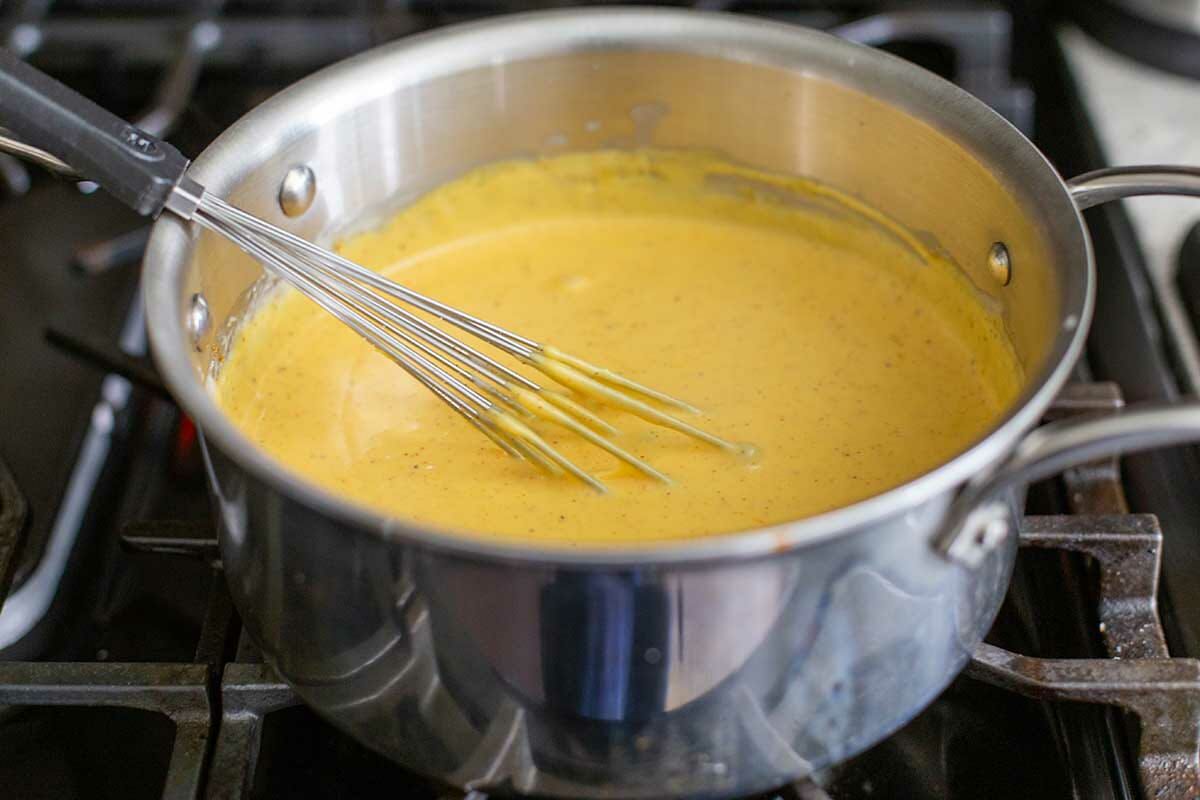 Whisking a cheese sauce in a saucepan on the stove to make Baked Cheesy Cauliflower.