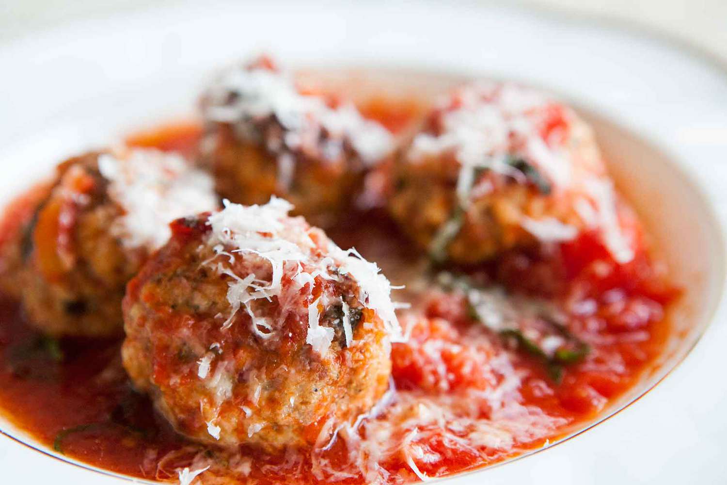 A plate of sausage meatballs with tomato sauce and parmesan cheese