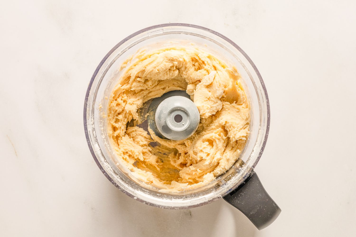 An overhead view of a food processor bowl with the wet and dry ingredients after processing for Sand Tarts recipe