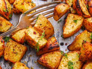 Close up of roasted potatoes in a baking pan, topped with fresh dill