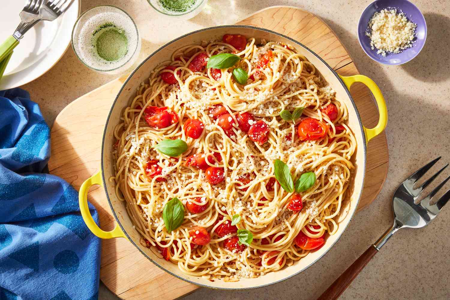 easy pasta pomodoro in a dutch oven on a wooden board at a table setting with glasses of carbonated water, bowl of parmesan, stack of plates, and a table napkin