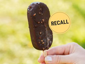 Hand holding a chocolatecovered ice cream bar next to a recall notice