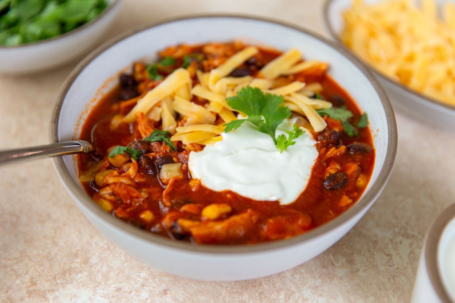 A bowl of chicken enchilada chili topped with shredded cheese sour cream and cilantro
