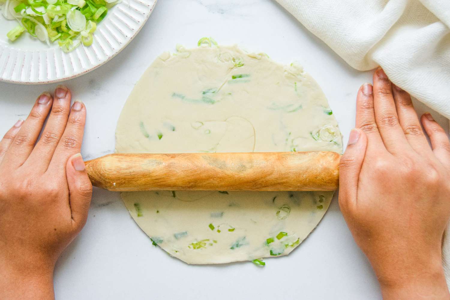 Rolling flattened scallion pancake with a rolling pin.