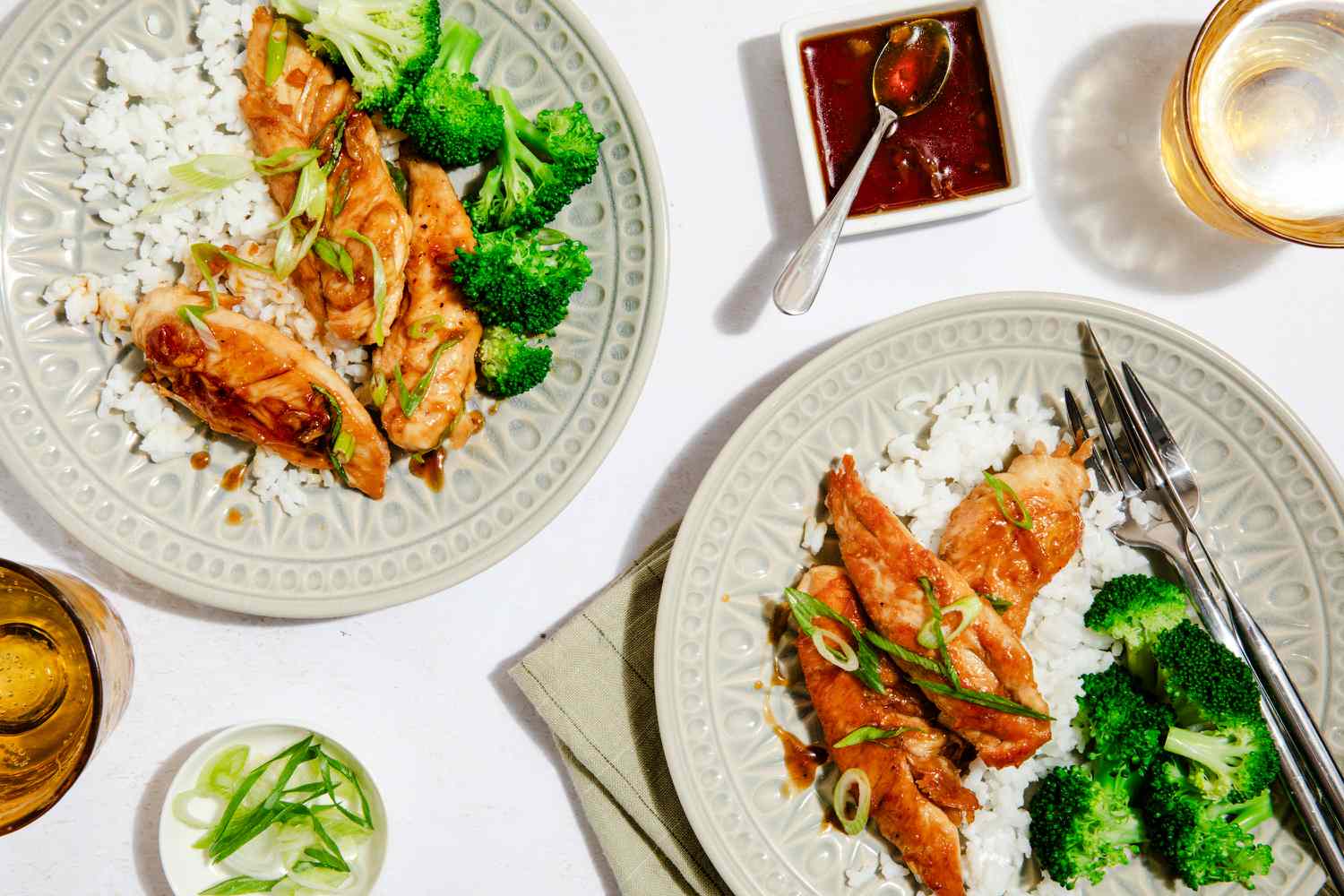 hot honey tenders served on two plates with broccoli and rice at a table setting with glasses of beer, a small bowl of sliced scallions, and more hot honey sauce in a small bowl