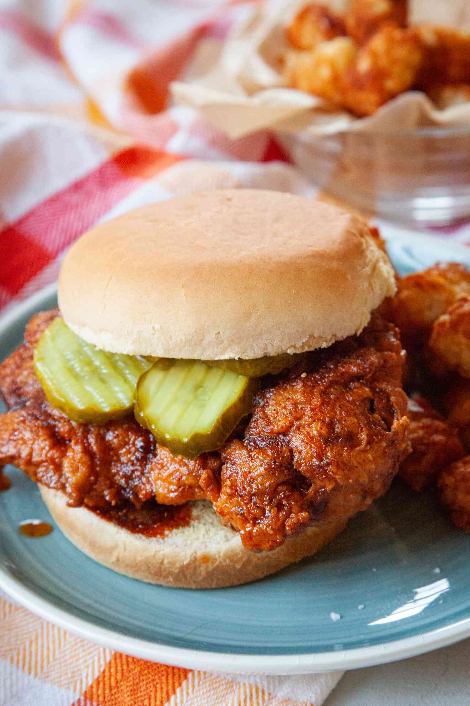 Nashville hot chicken sandwich with pickles and served on a plate.