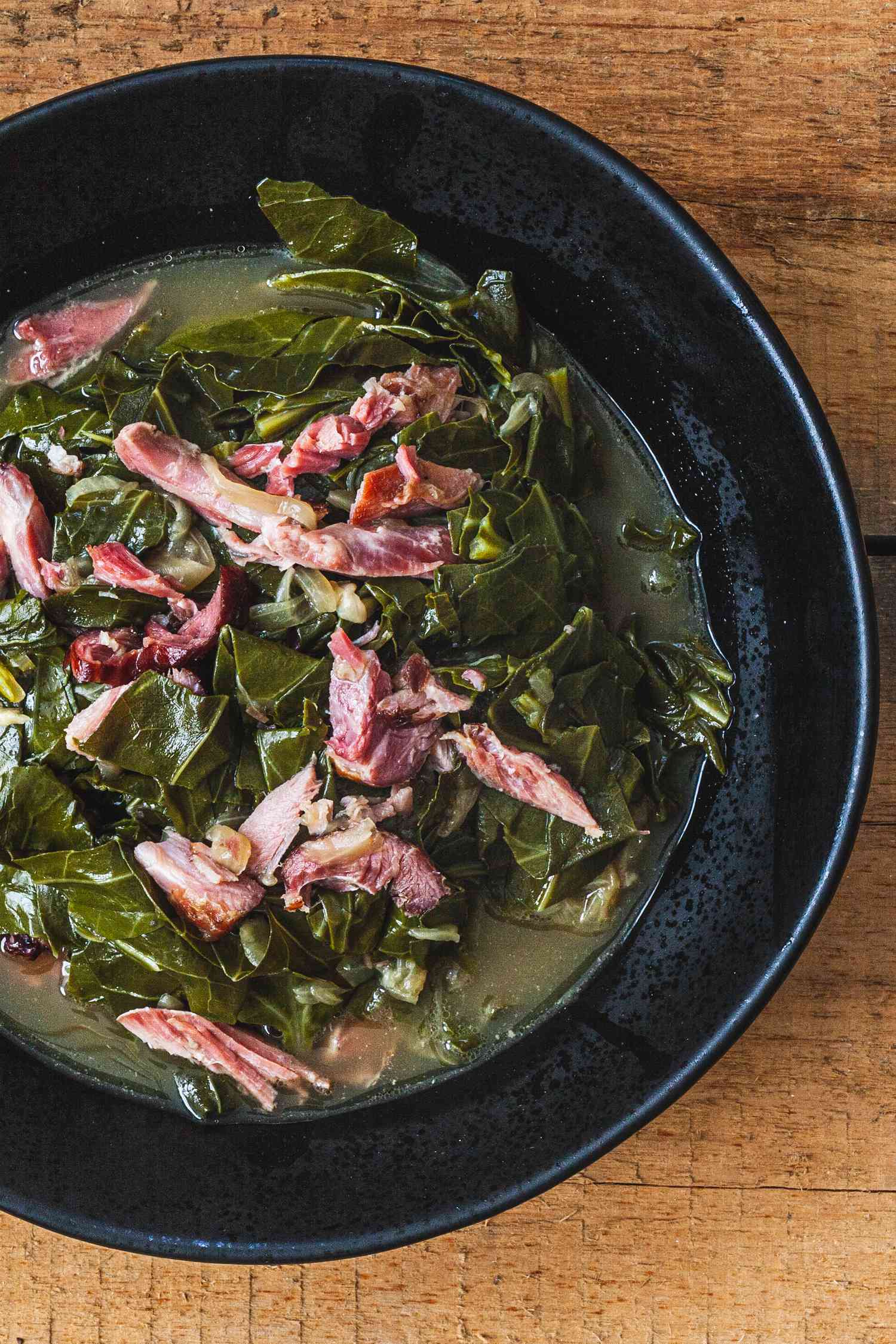 Overhead view of southern collard greens in a black bowl on a wood surface.