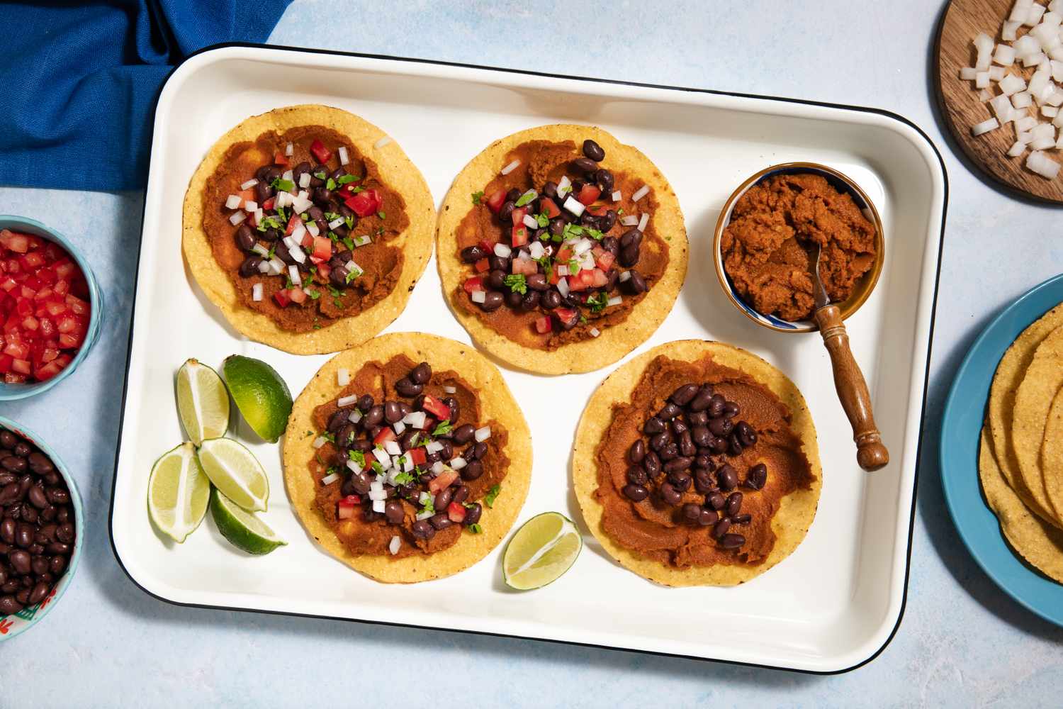 Tray of pumpkin and black bean tostadas with bowls of diced vegetables and lime wedges