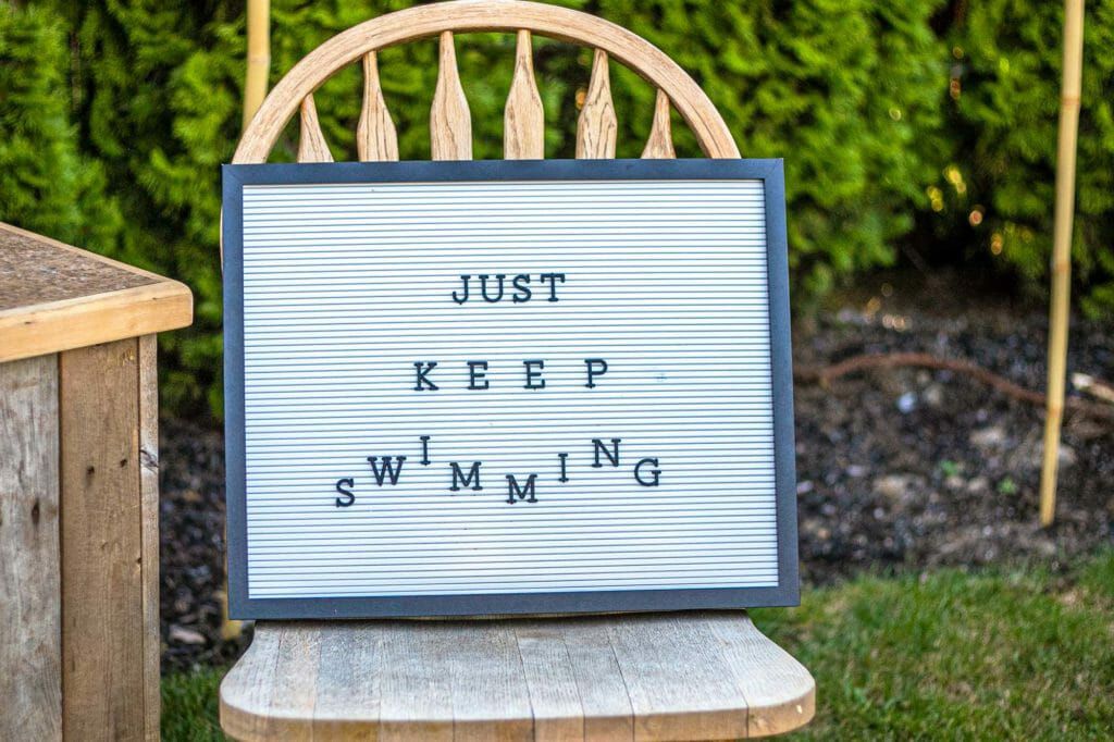 A sign that reads "Just Keep Swimming" set on a chair outside as part of the backyard family activities.