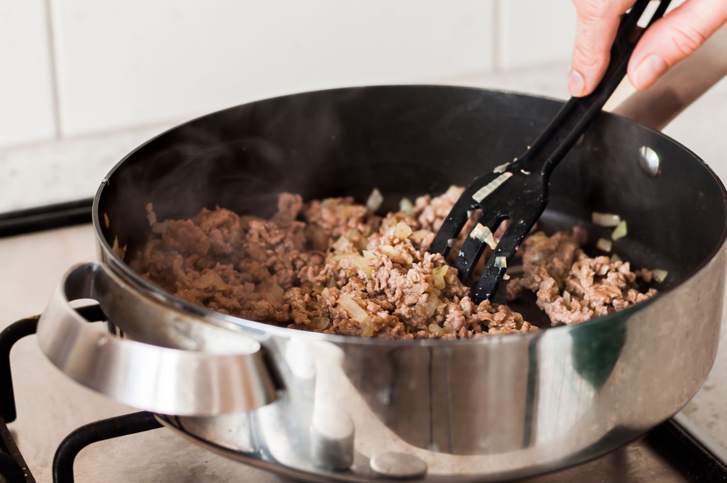 Cooking ground beef with onions in a pan being stirred with a black spatula