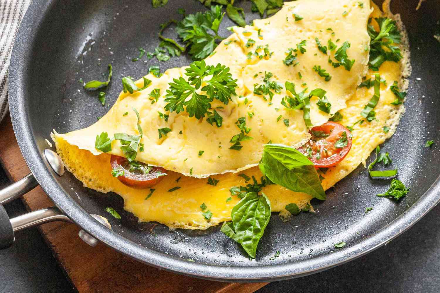 Cooked omelette with cherry tomatoes and parsley in a pan resting on a cutting board