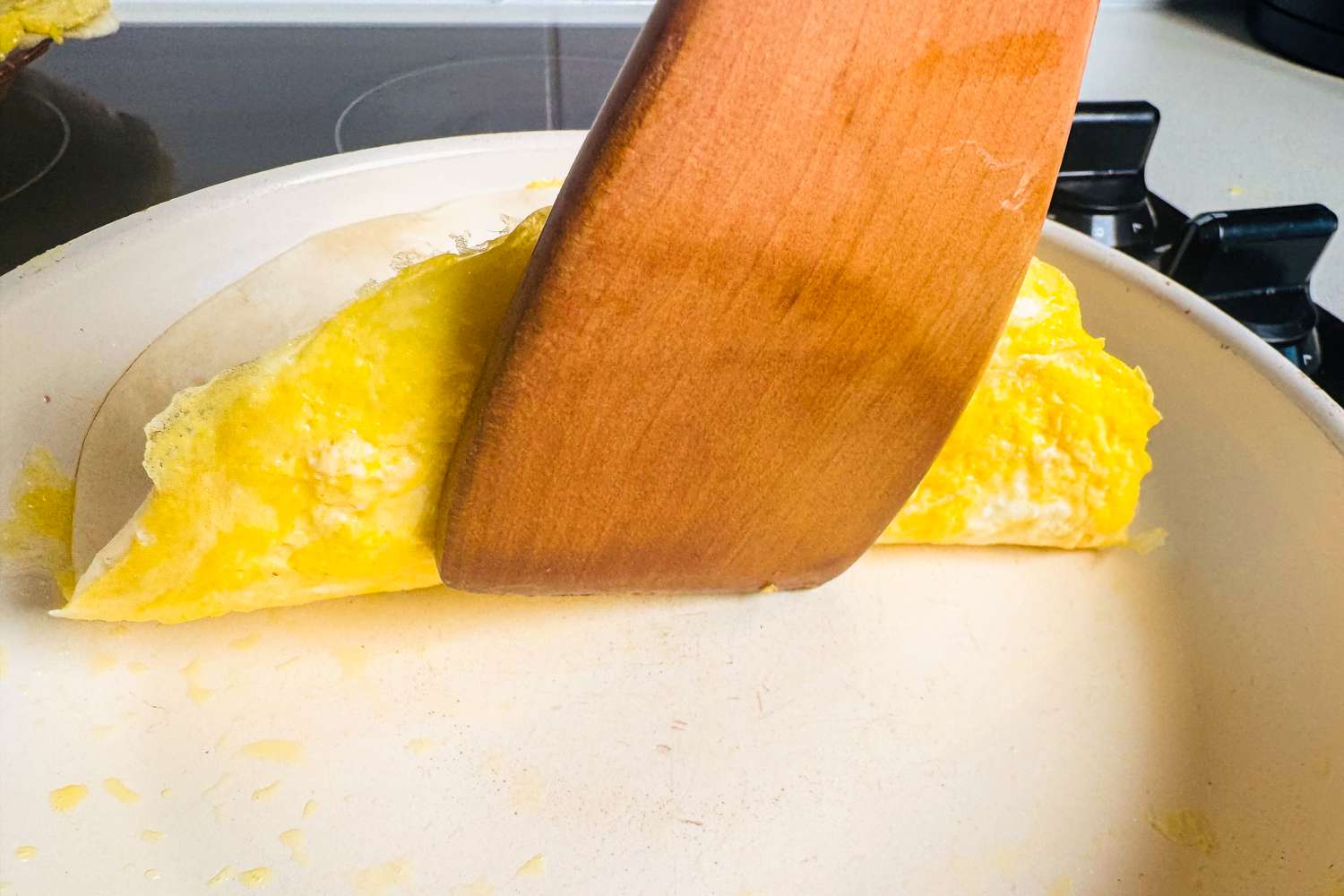 Tortilla being folded over scrambled eggs in a skillet with a wooden spatula.