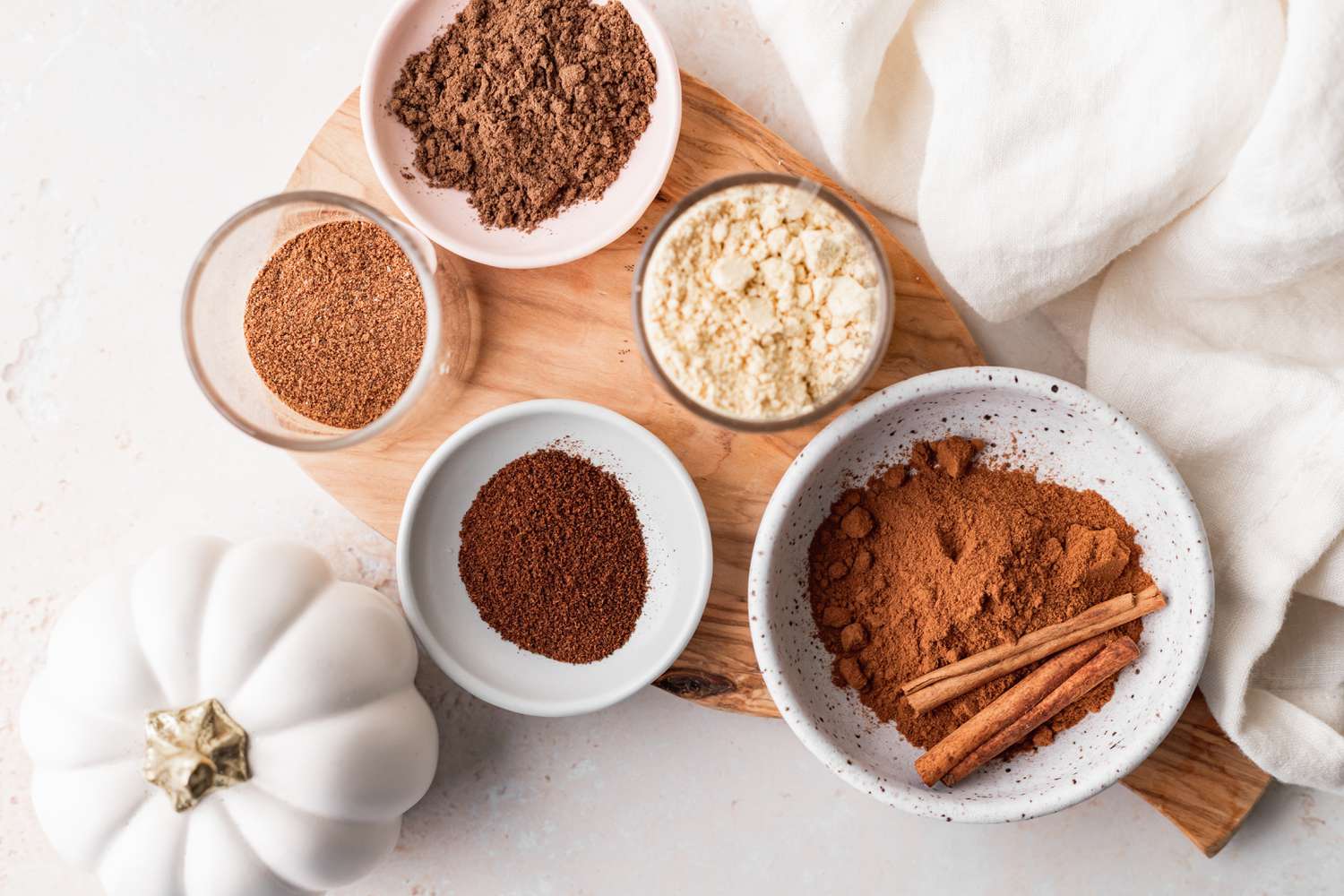 Overhead view of small bowls of individual spices set on a wooden cutting board to show how to make pumpkin pie spice.