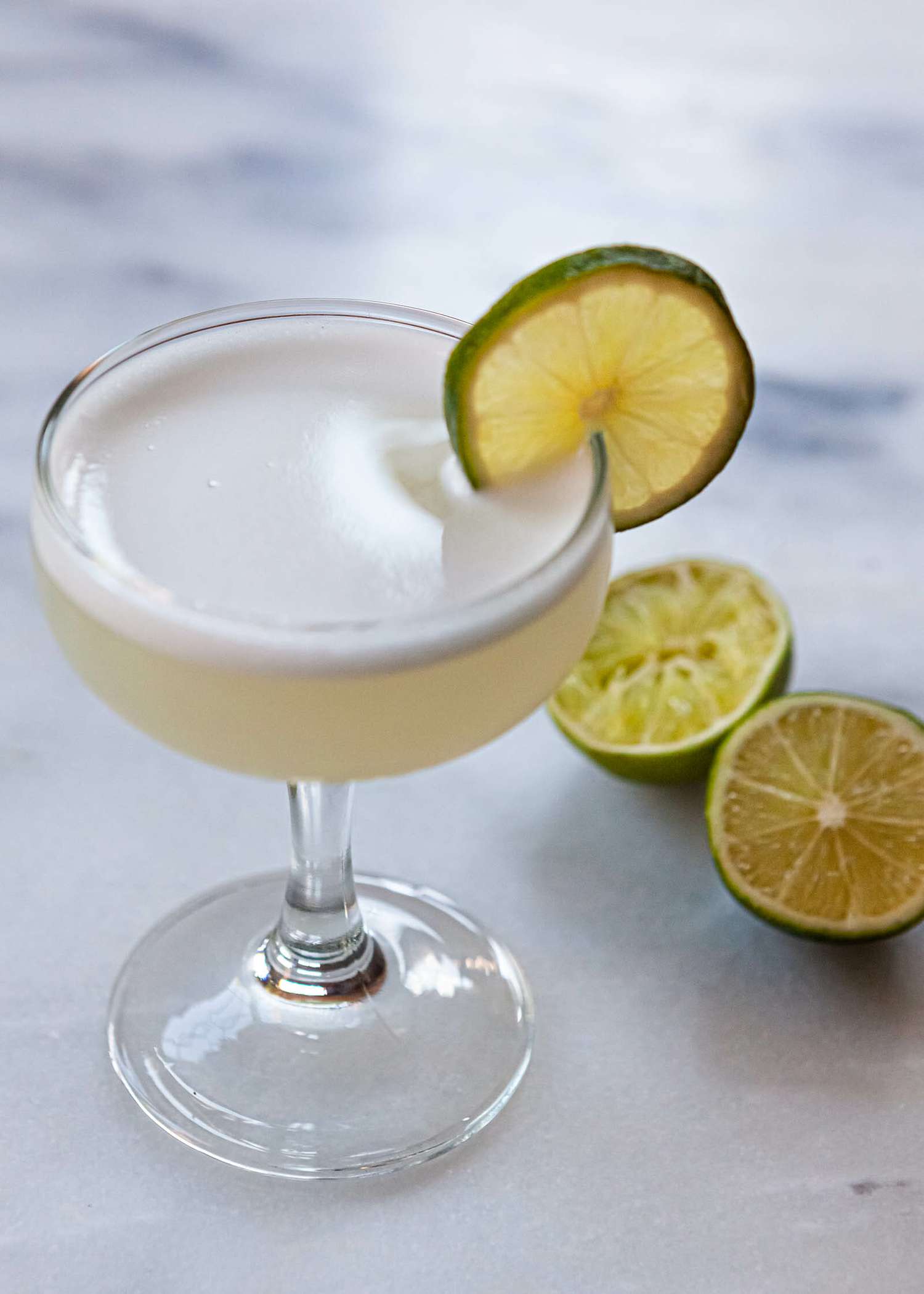 Gin gimlet in a coupe glass with a lime wedge on the side and halved lime next to the glass.