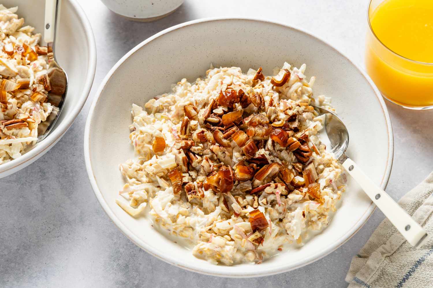 Overhead shot of a bowl of muesli with milk and a spoon, with a glass of orange juice in the background