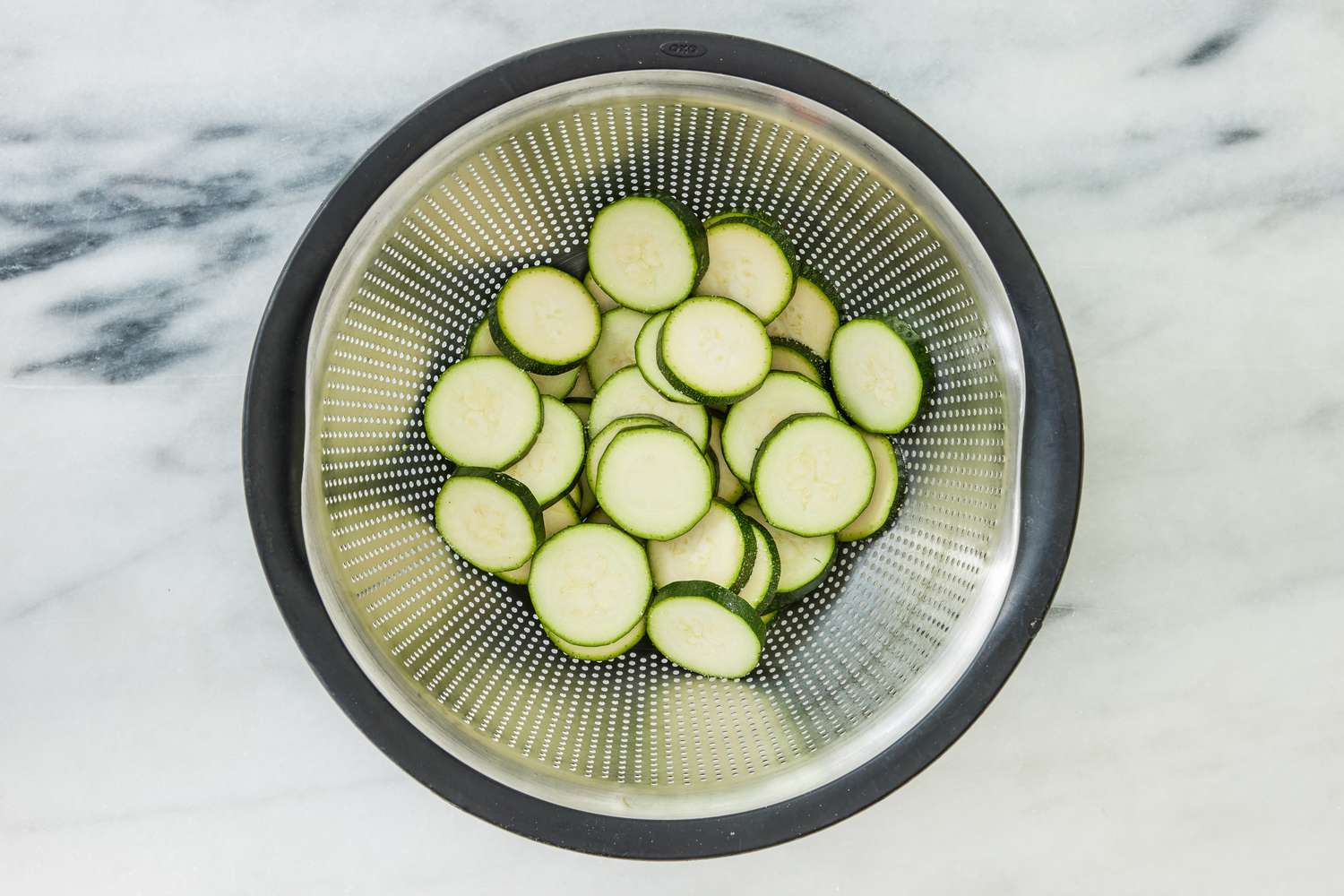 salted zucchini slices in a colander for crispy chicken thighs with zucchini and shallots recipe