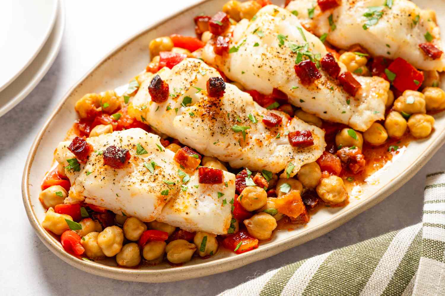 Cod fillets served on a bed of chickpeas and diced vegetables garnished with herbs and spices