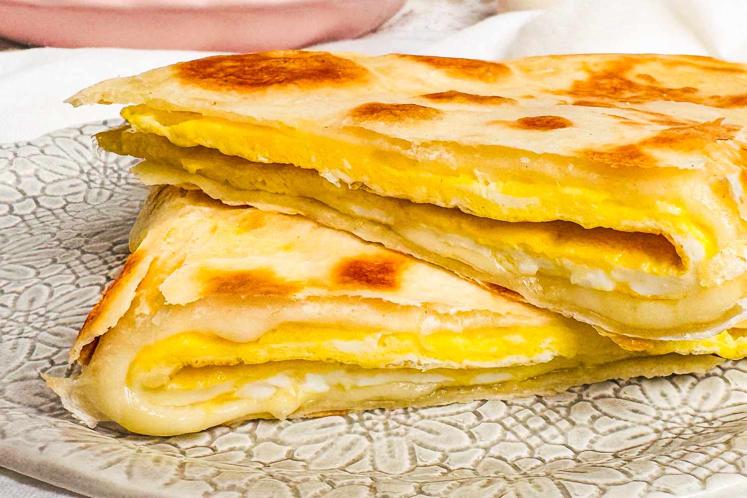 Egg and cheese tortilla folded and stacked on a plate.