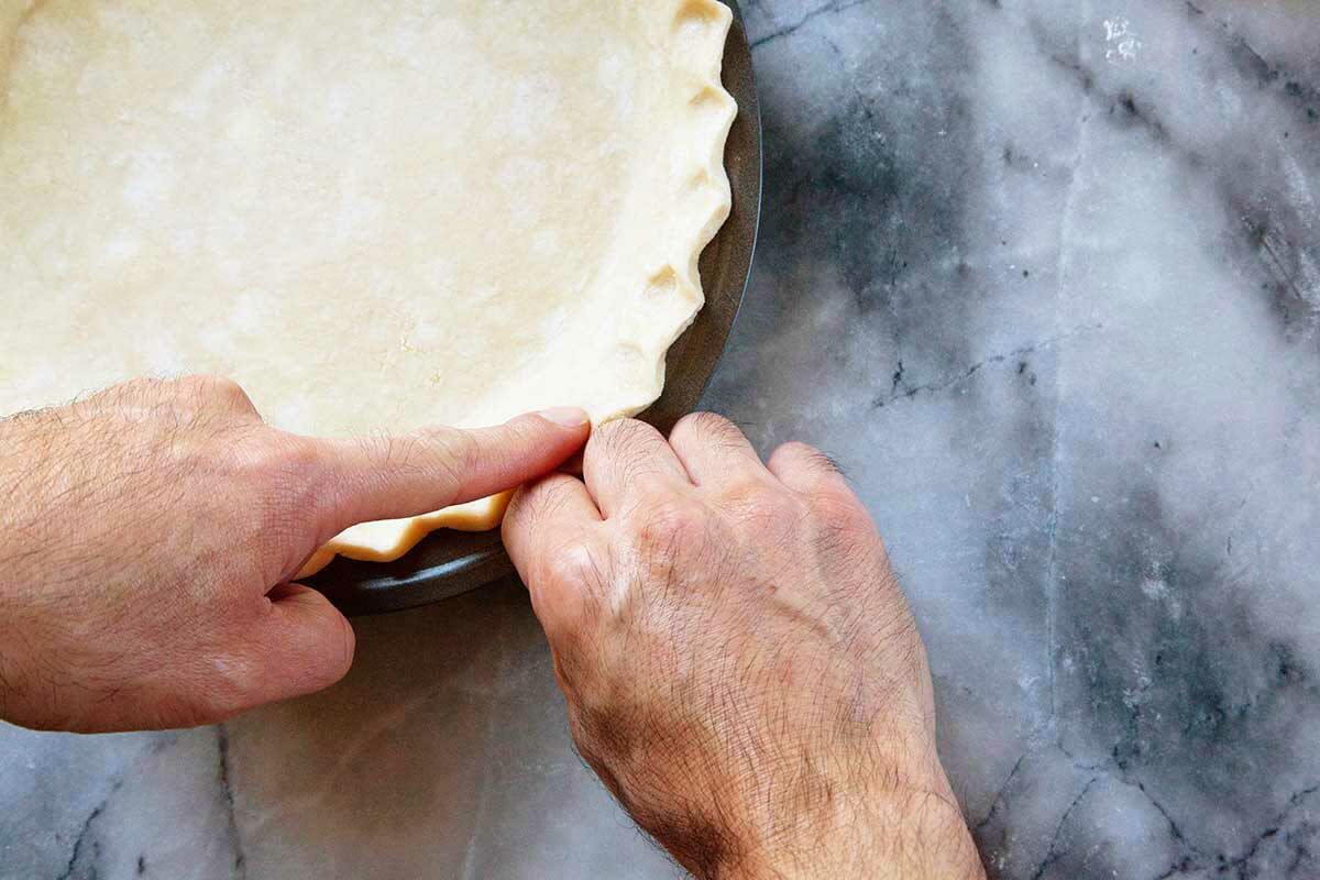 Pennsylvania dutch shoofly pie crust being crimped at the edges by two hands.