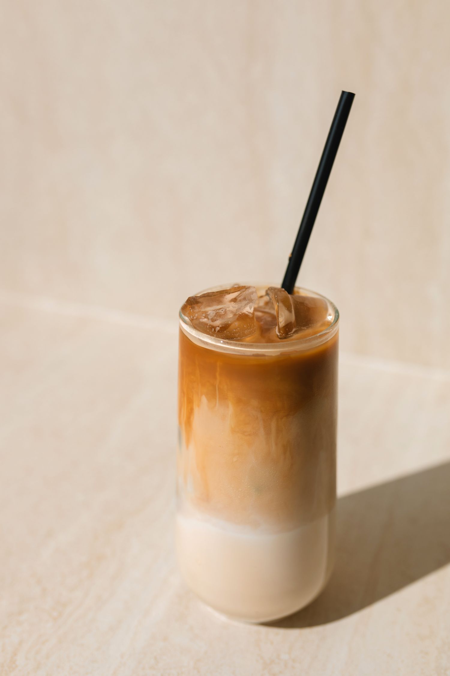 A glass of iced latte with a straw on a lightcolored surface