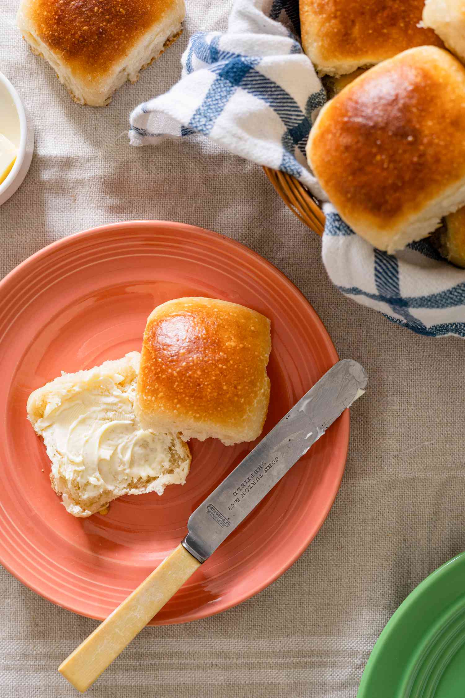 A Sourdough Roll Cut in Half on a Plate with Smeared Butter Next to a Basketful of Sourdough Rolls and One on the Counter