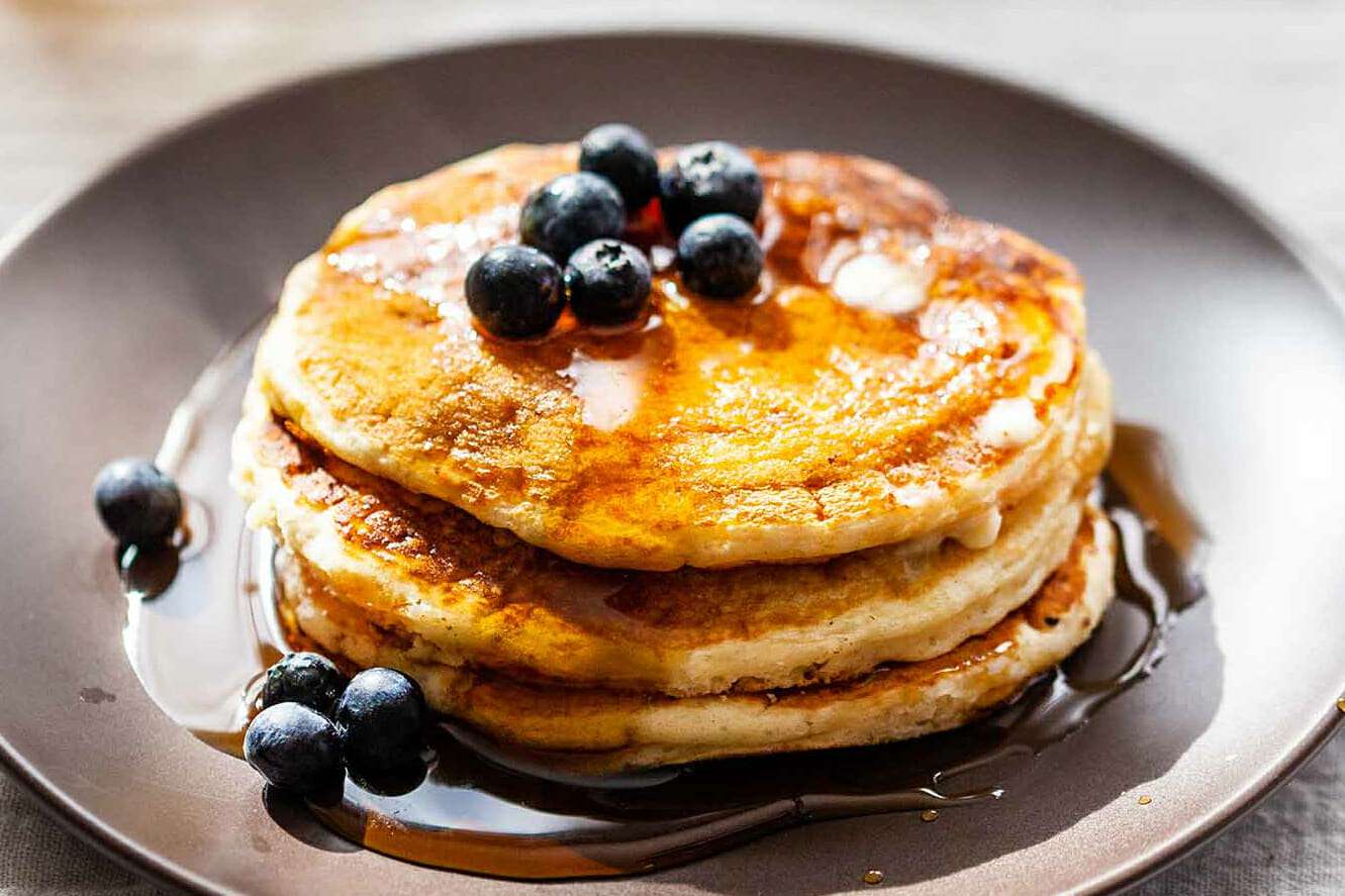 buttermilk pancakes topped with blueberries and syrup on a gray plate