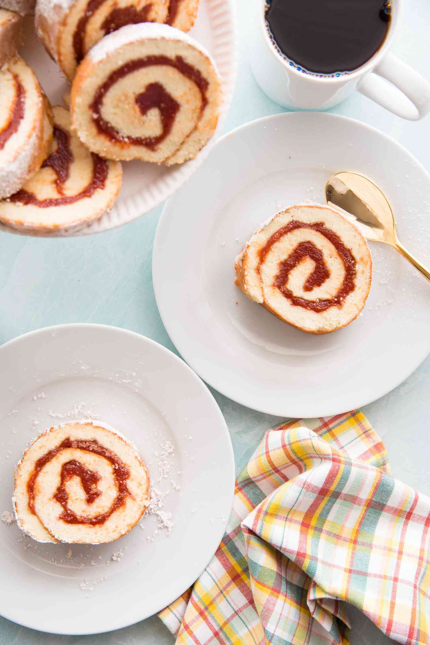 Guava Jelly Roll Cake on two plates with more slices set behind it on a cake stand.