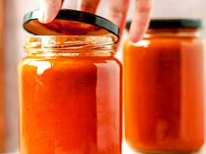 Jar of tomato sauce being opened by a hand another jar in the background