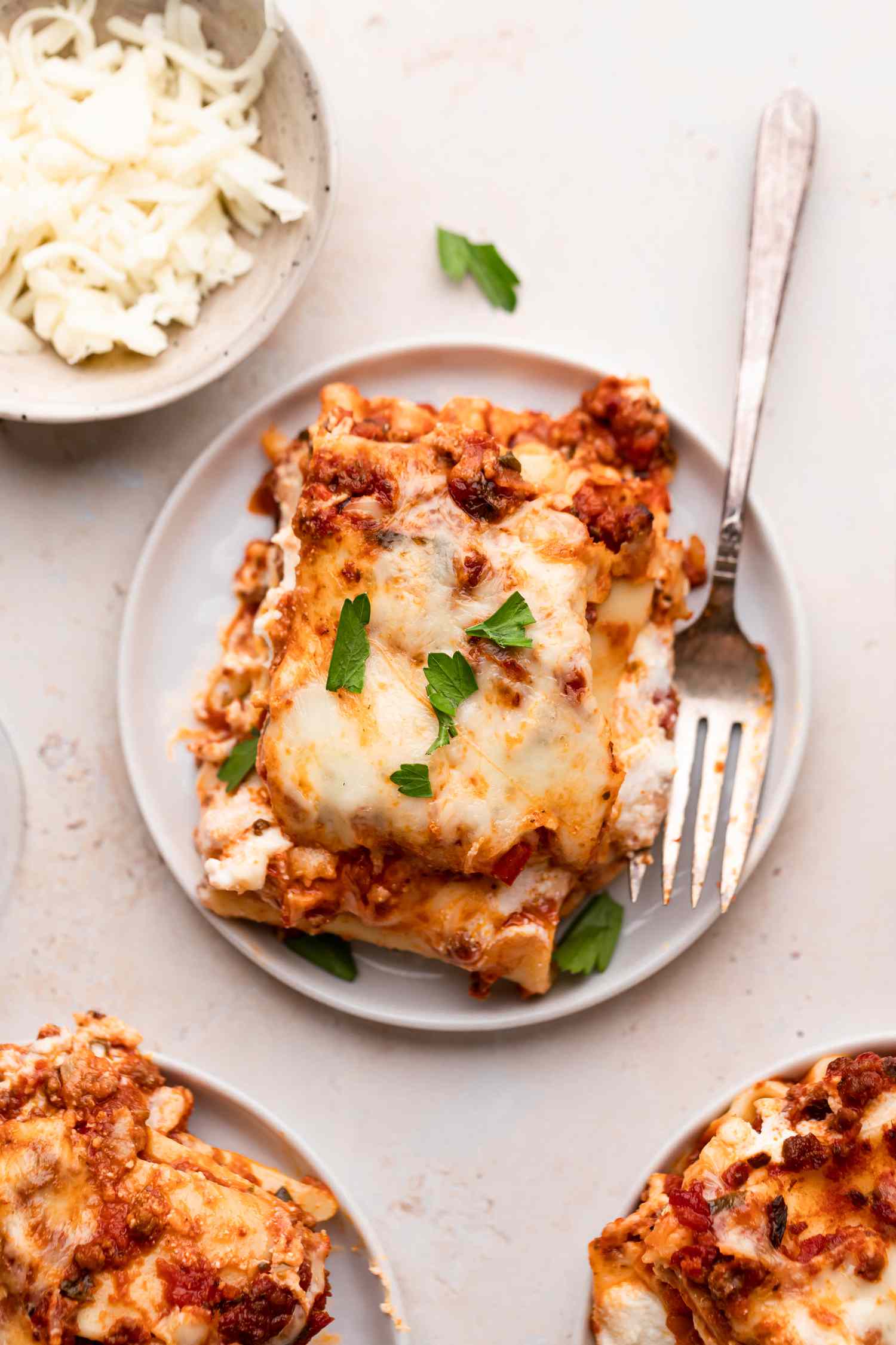 Overhead view of a piece of lasagna on a plate with cheese set next to it.