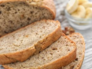 Sliced banana bread on a table with a bowl of banana slices in the background
