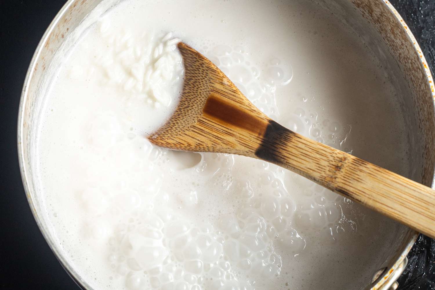Coconut Milk, Water, and Rice in a Pot with a Wooden Spoon