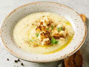 A bowl of creamy soup topped with roasted cauliflower and garnished with herbs
