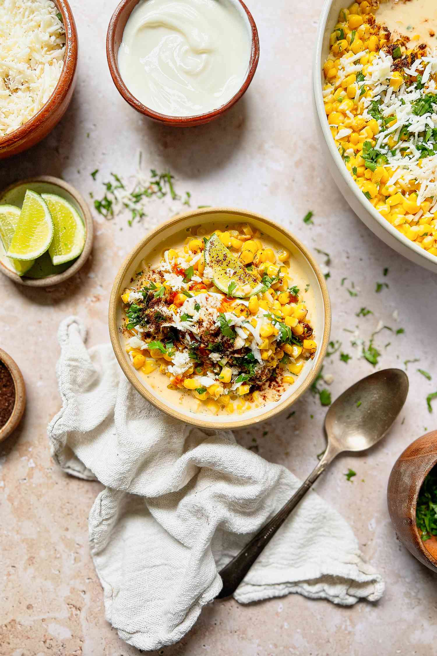 Bowl of Esquites Topped with Cilantro, Cotija Cheese, and Ancho Chile Pepper Surrounded by Bowls of Toppings