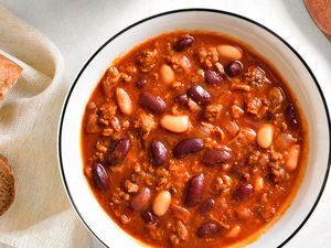 Bowl of chili with kidney and white beans on a table with bread and a spoon