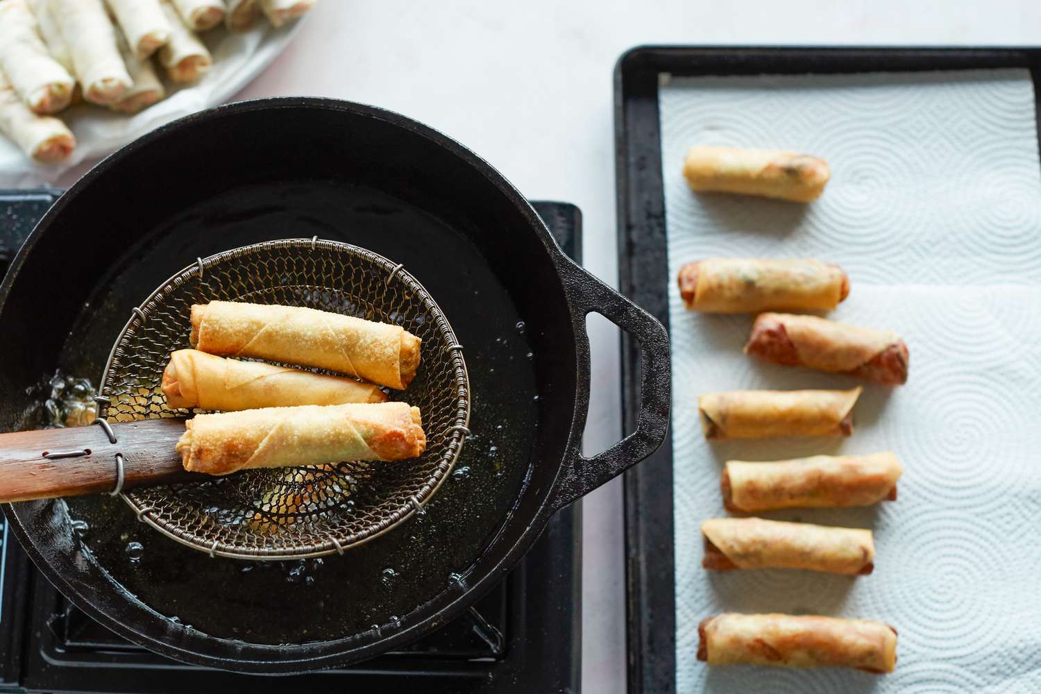 Overhead view of spring rolls frying in a skillet.