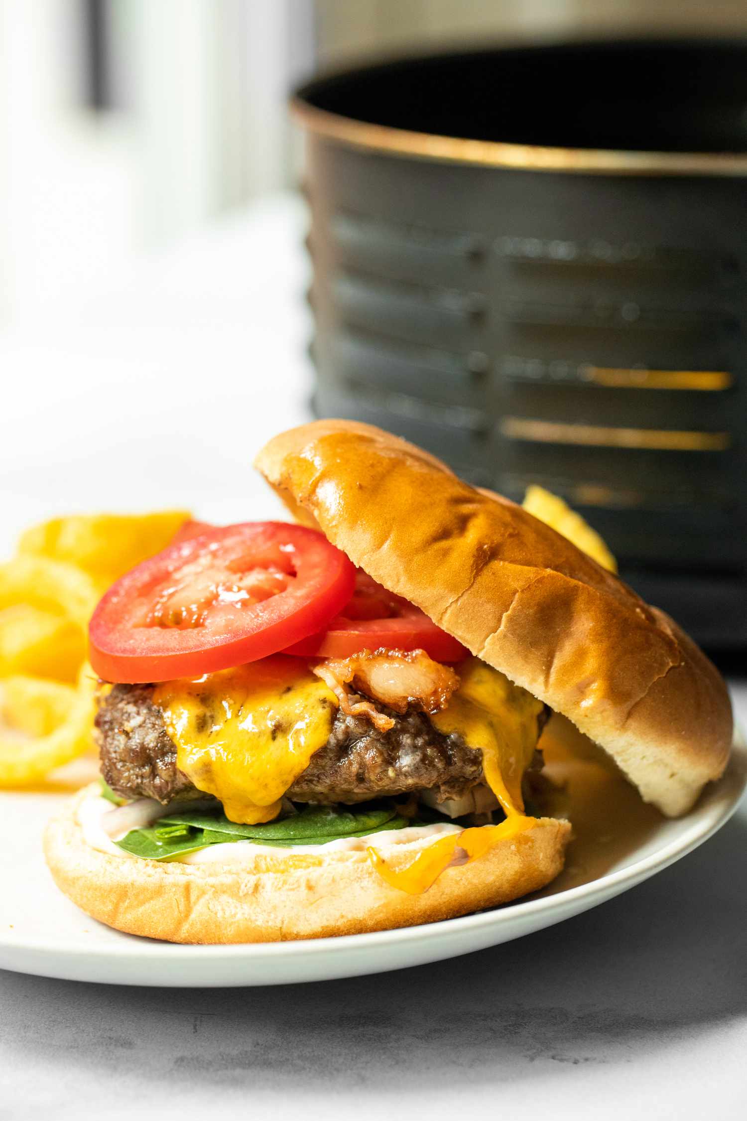 Air Fryer Burger with Onion Rings on a Plate with an Air Fryer Basin in the Background