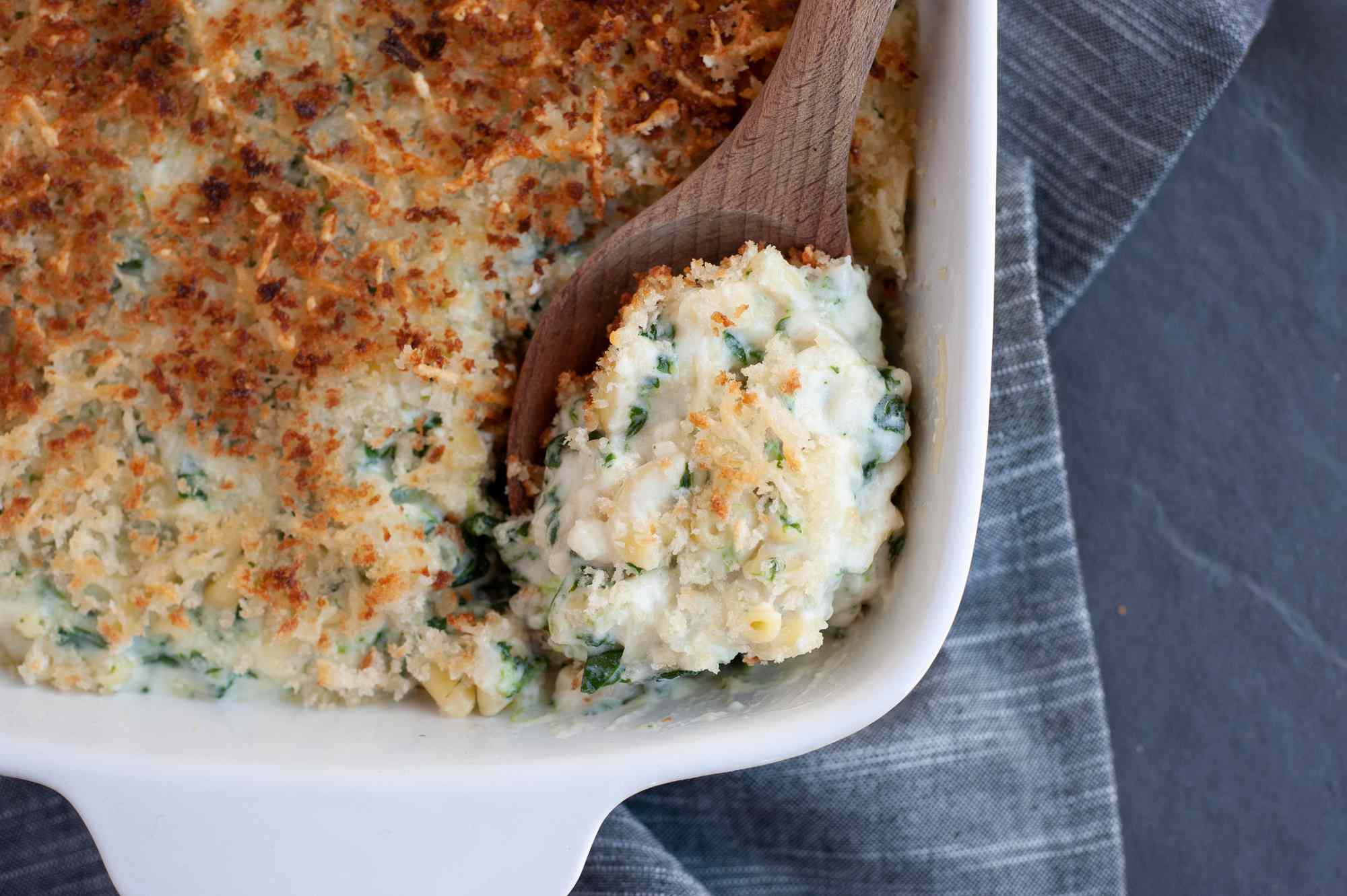 Scooping a spoonful of mac and cheese with creamed spinach out of a casserole dish.