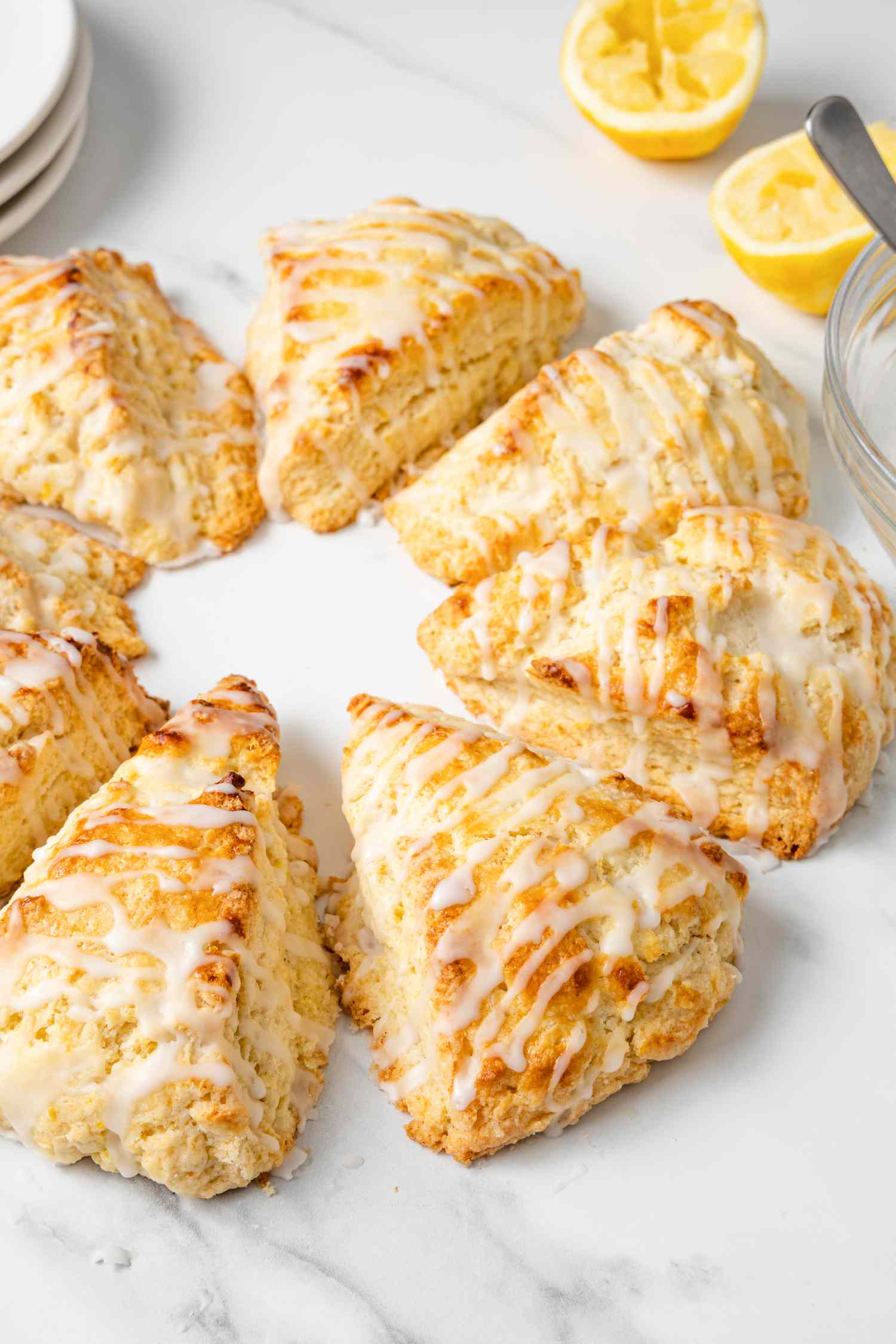 Lemon Scones with Lemon Glaze Surrounded by Plates, Half Lemons, and Bowl