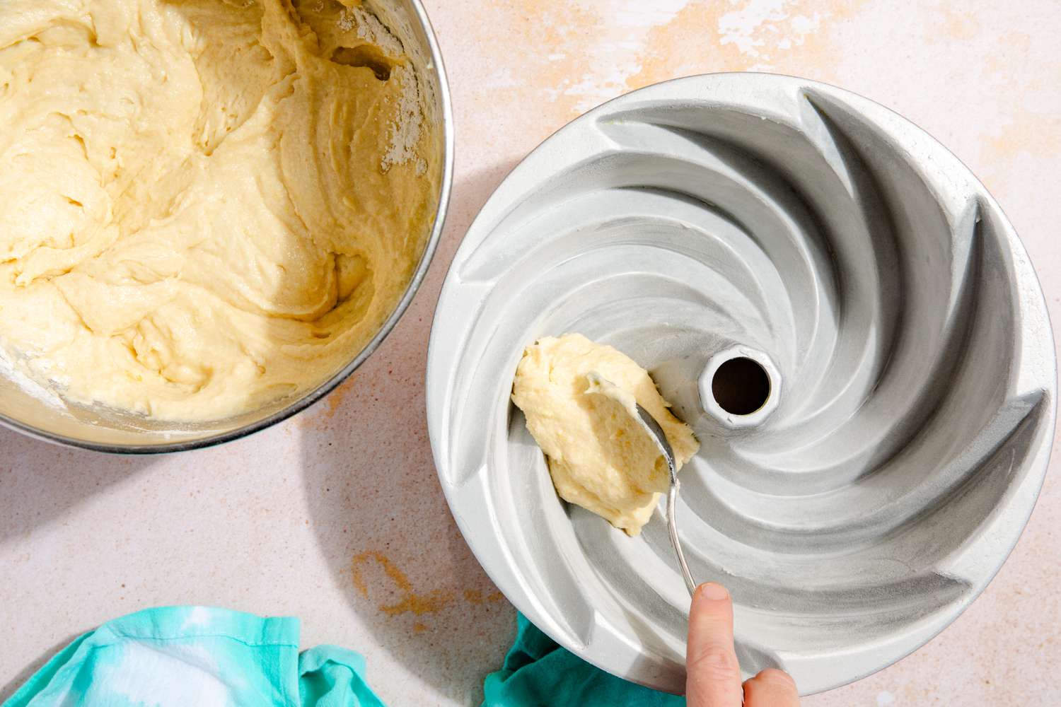 A hand adding a spoonful of batter to a greased bundt pan