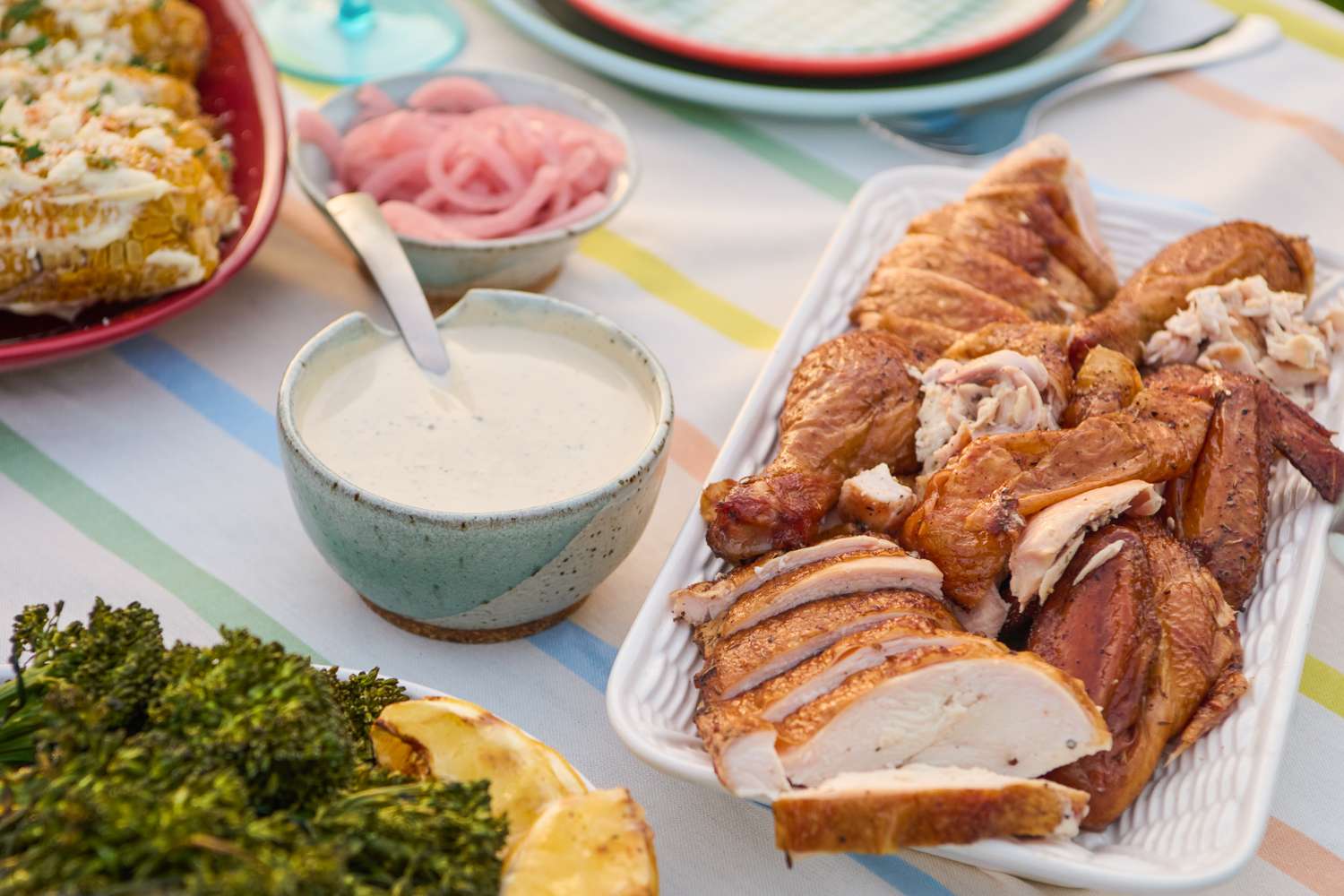 Platter of sliced grilled chicken with a bowl of white sauce on a summer-themed table setting